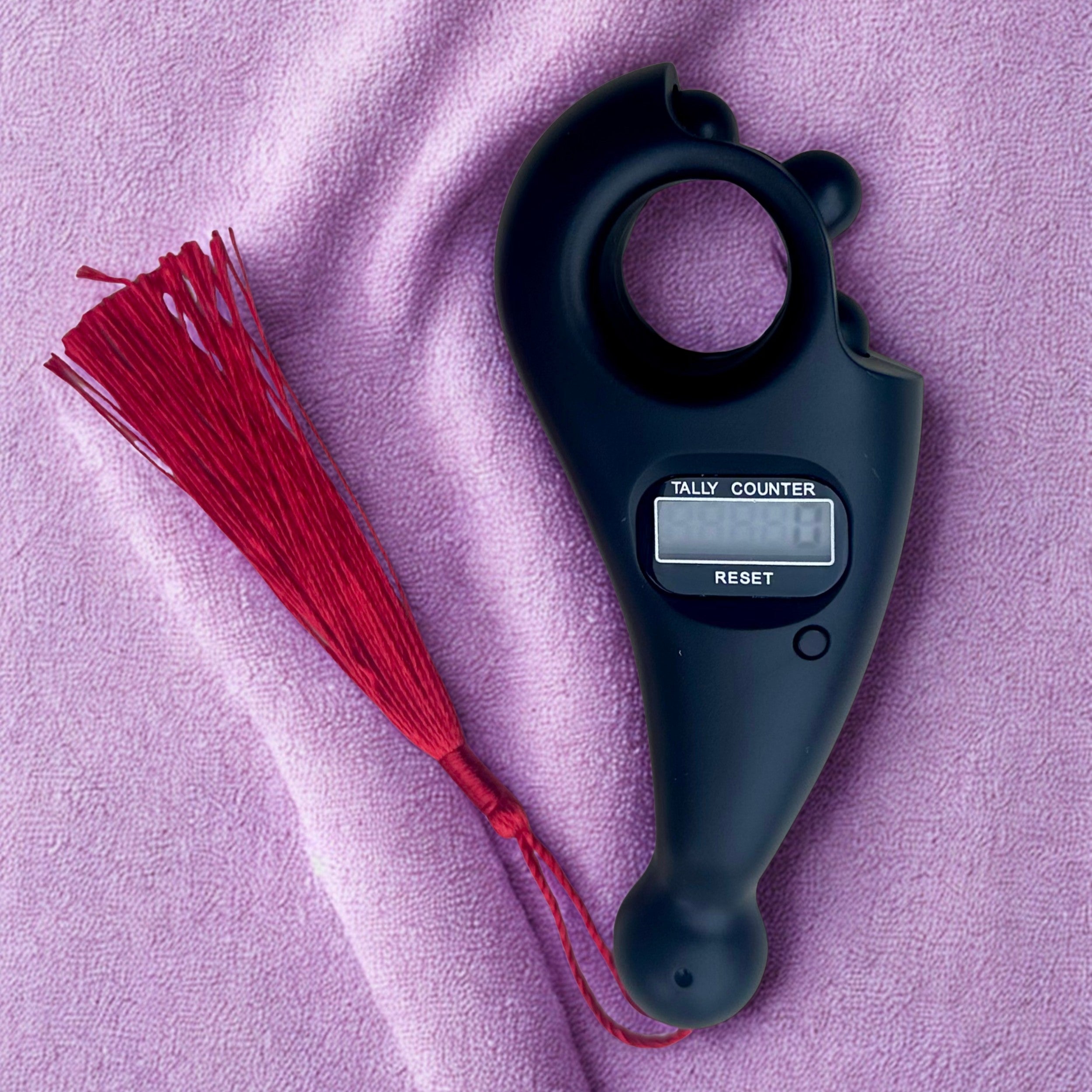 Black tally counter with red tassel on a pink fabric background
